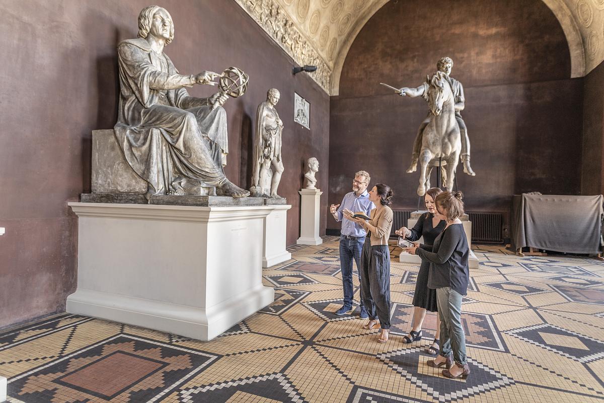 Fire personer står ved Copernicus skulpturen i forhallen