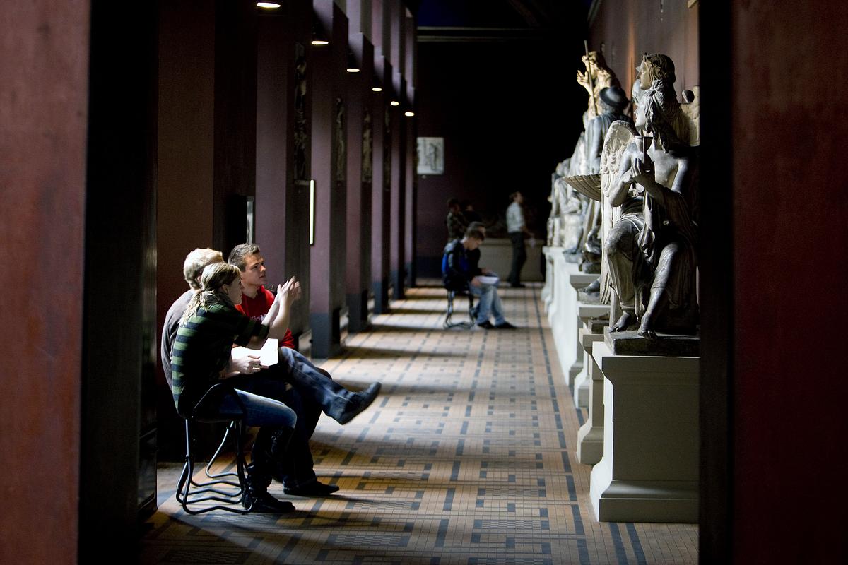 Tre elever sidder og ser på skulpturer i korridoren