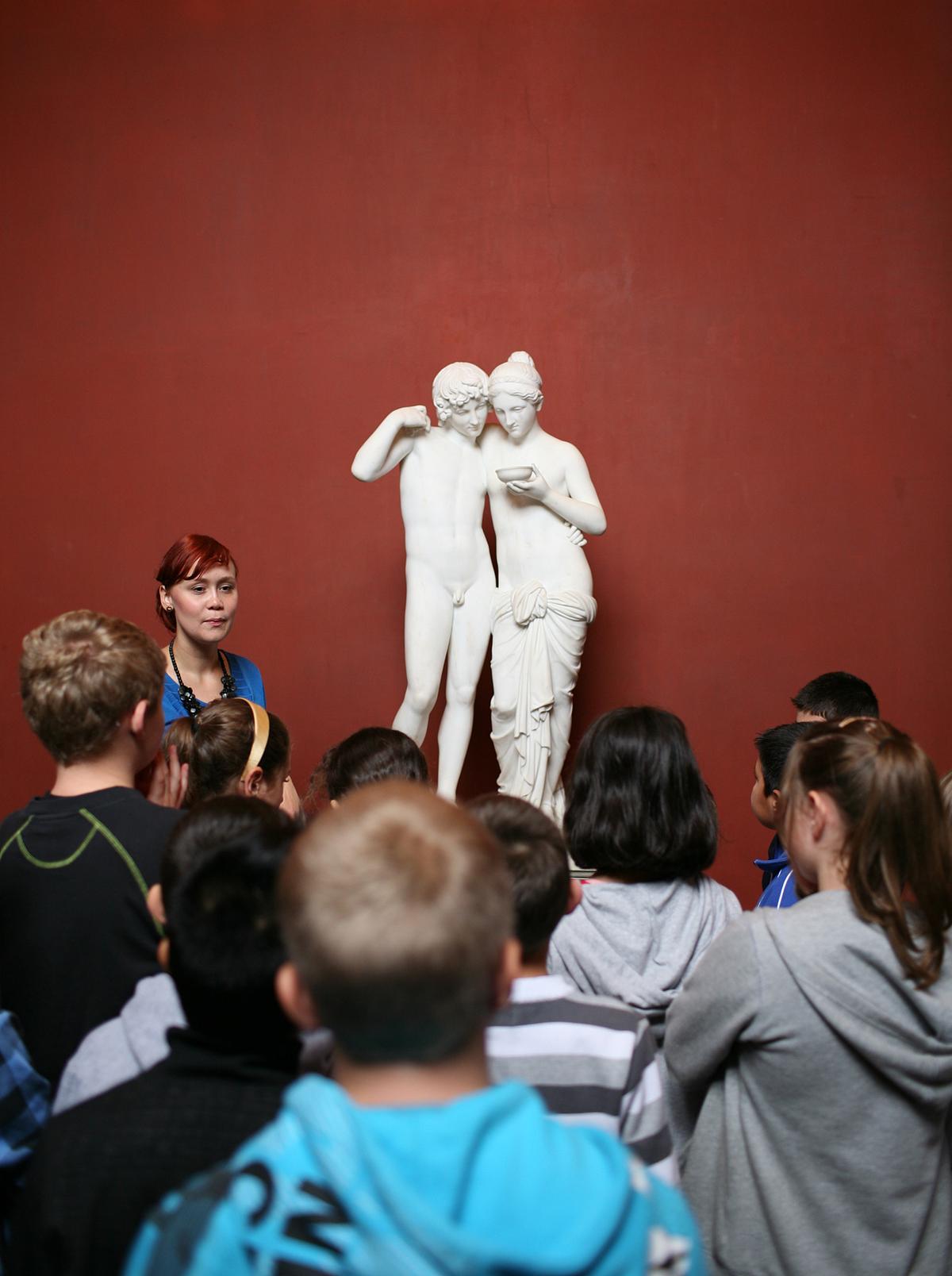 Skoleelever står foran skulptur og lytter til underviser