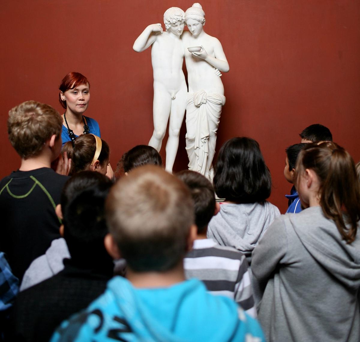 Skoleelever står foran skulptur og lytter til underviser