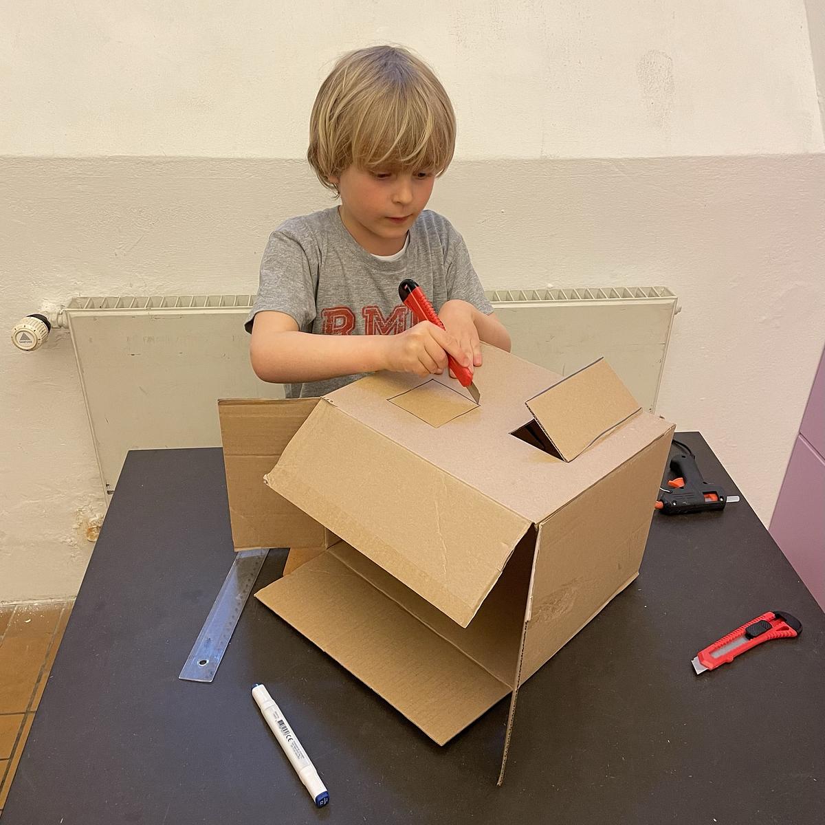 Dreng der udskærer firkanter i en papkasse