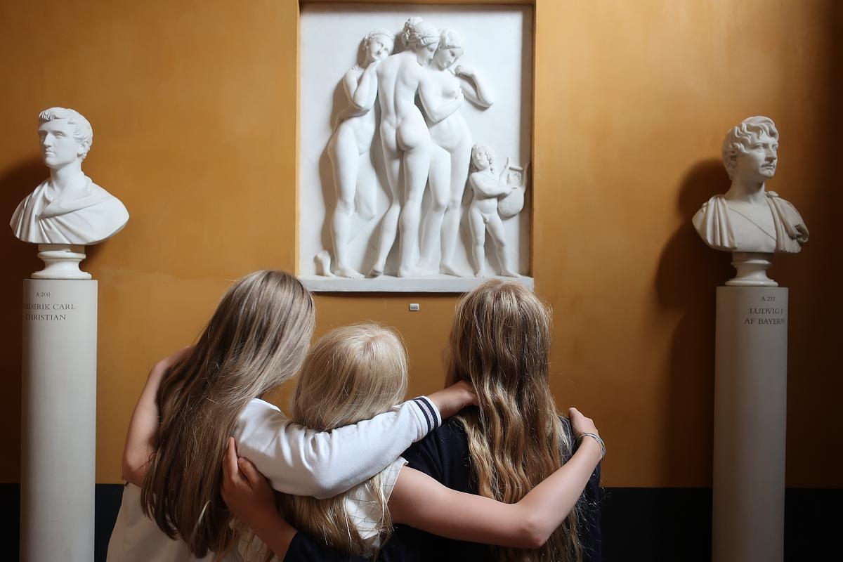 Tre børn med armene om hinanden kigger på relief